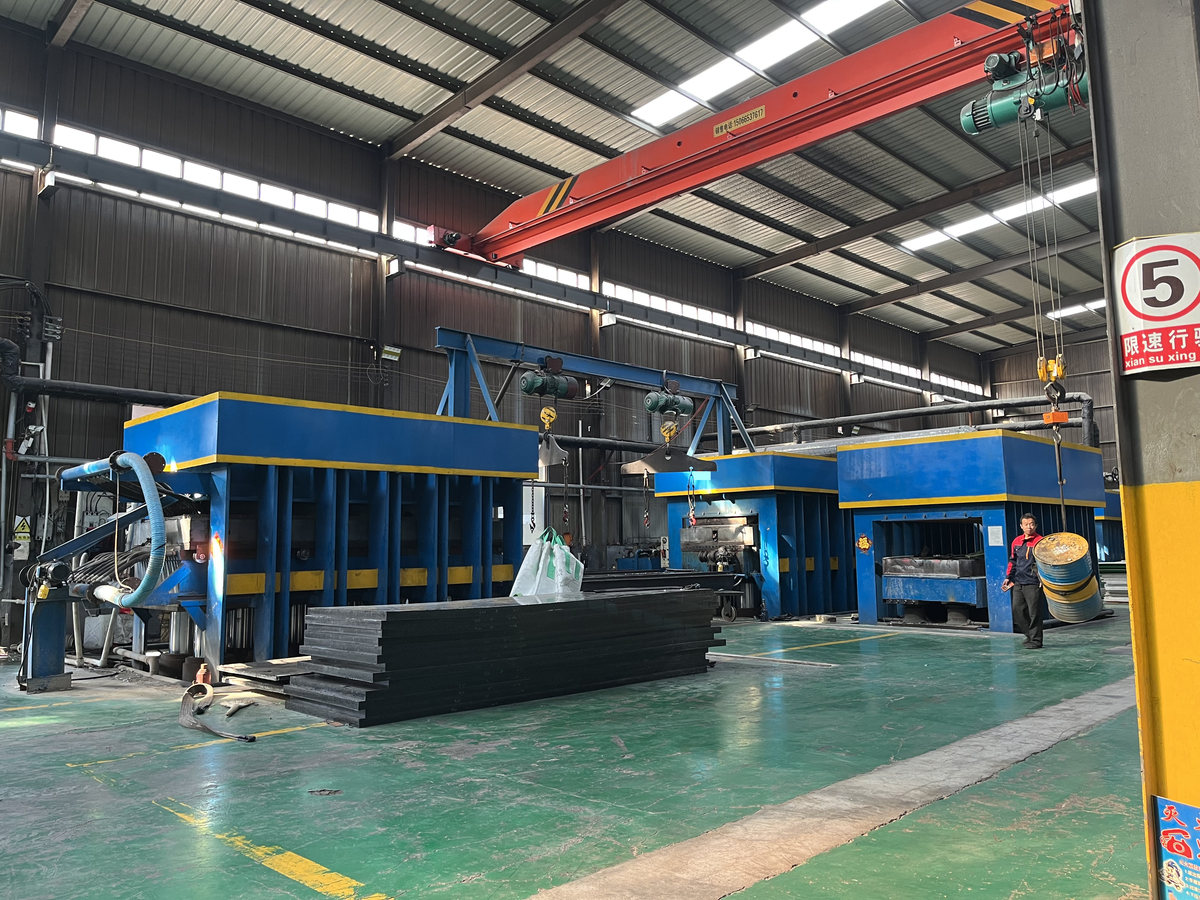 Press workshop at the Matunion factory — hydraulic presses, overhead crane and stacked HDPE sheets
